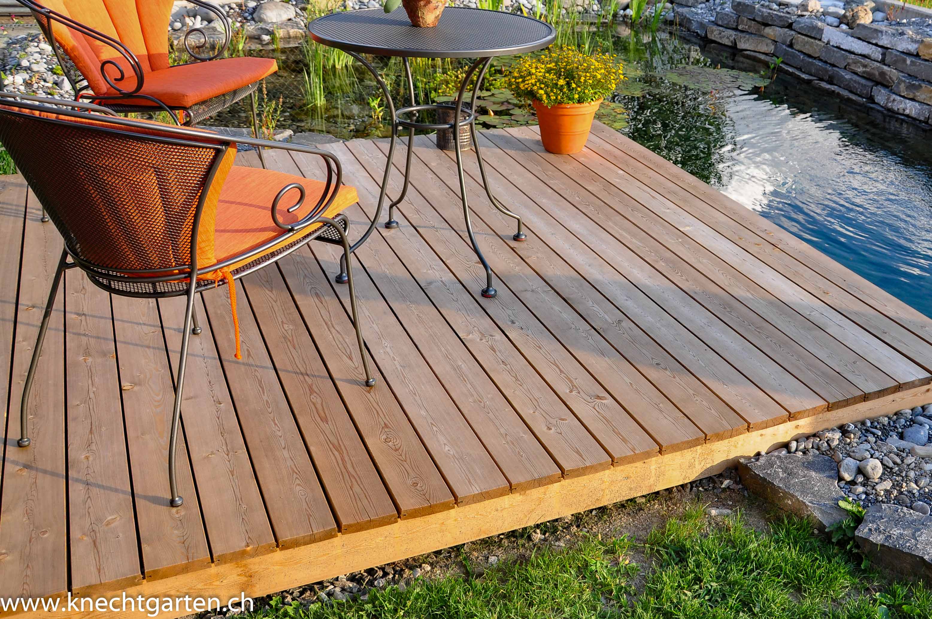 Holzdeck mit Gartenmöbel neben Schwimmteich