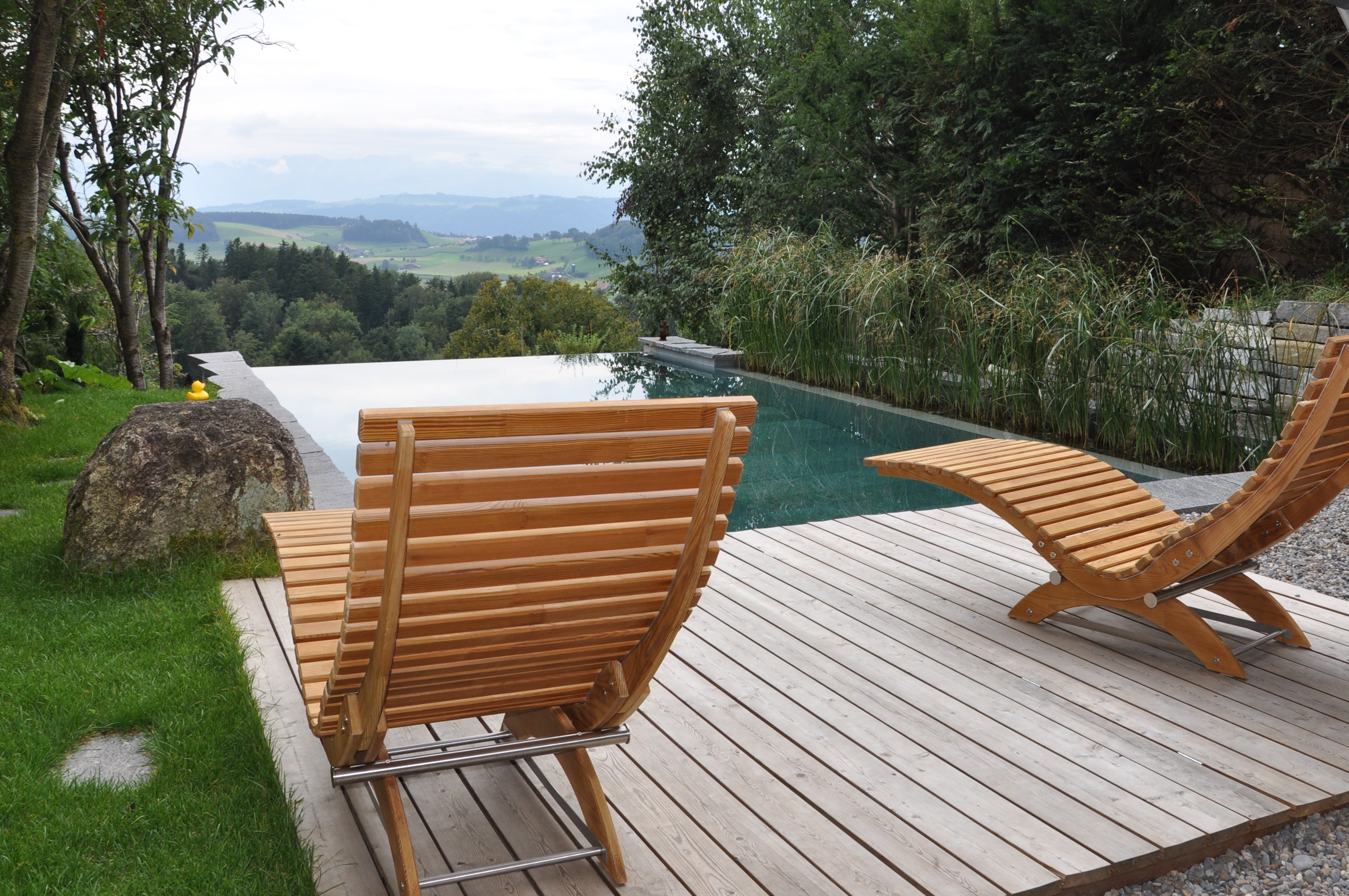 Hellbraune Holz-Liegestühle auf Holzdeck vor Infinity Pool mit schöner Aussicht